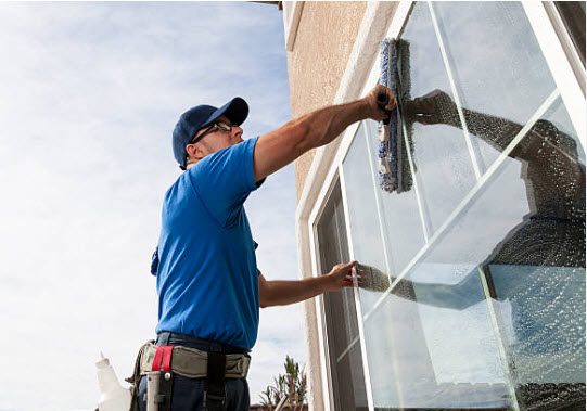 A gulf south janitorial technician in blue shirt and hat cleaning window.