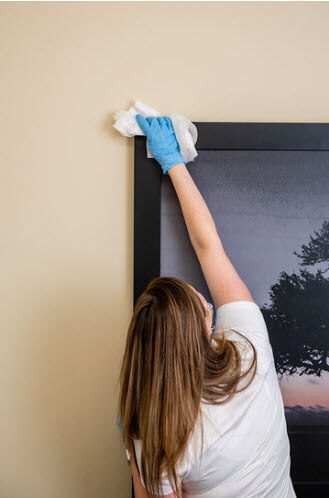 A woman in blue gloves cleaning the wall.