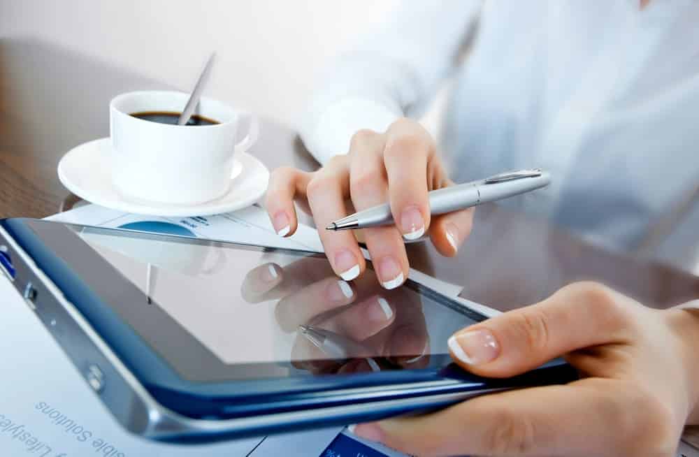 A person using a tablet with pens and coffee.