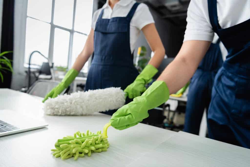 Two people wearing green gloves and cleaning a table.