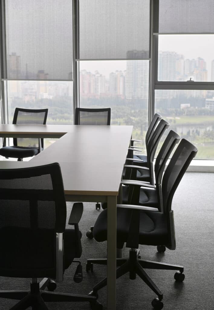 A conference table with chairs in front of windows.