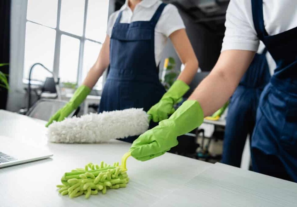 Two people wearing green gloves and cleaning a table.