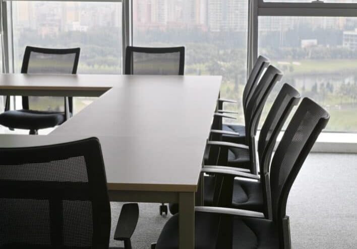 A conference table with chairs in front of windows.