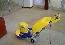 A yellow and blue low moisture carpet cleaning machine is being used by a Gulf South Janitorial Technichian